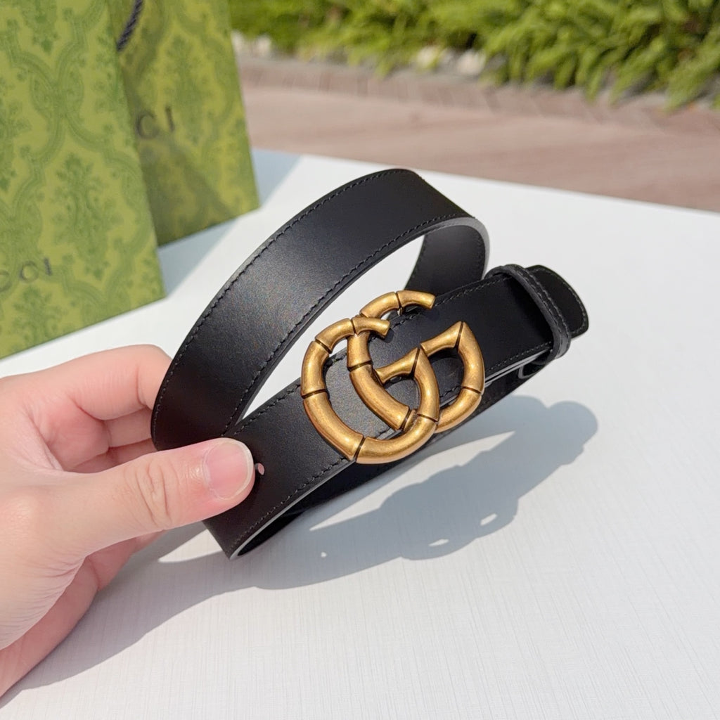 Gucci leather belt, dark black strap with gold-tone interlocking buckle, held up for view