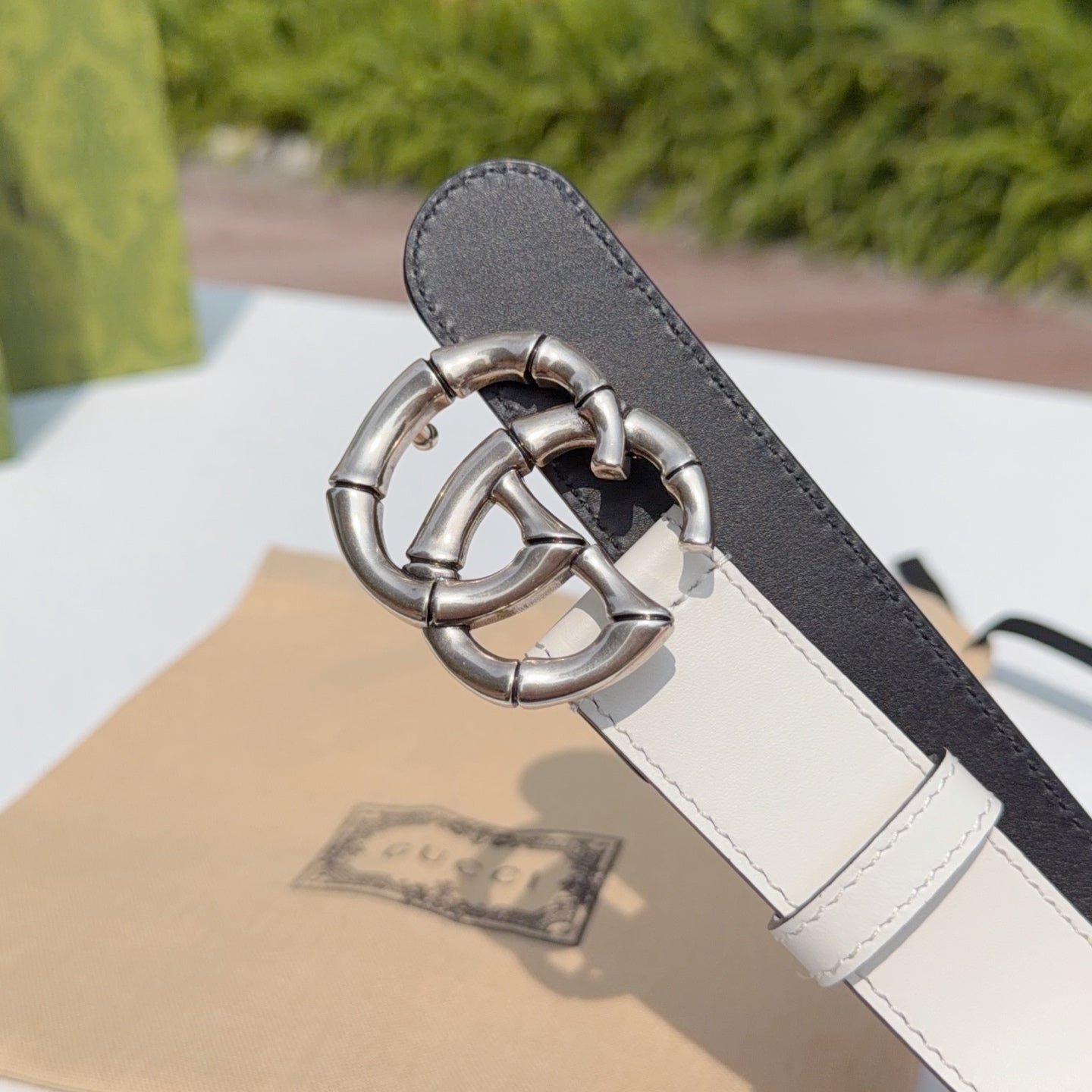Cream-and-dark leather belt with silver-tone double G buckle, close-up end