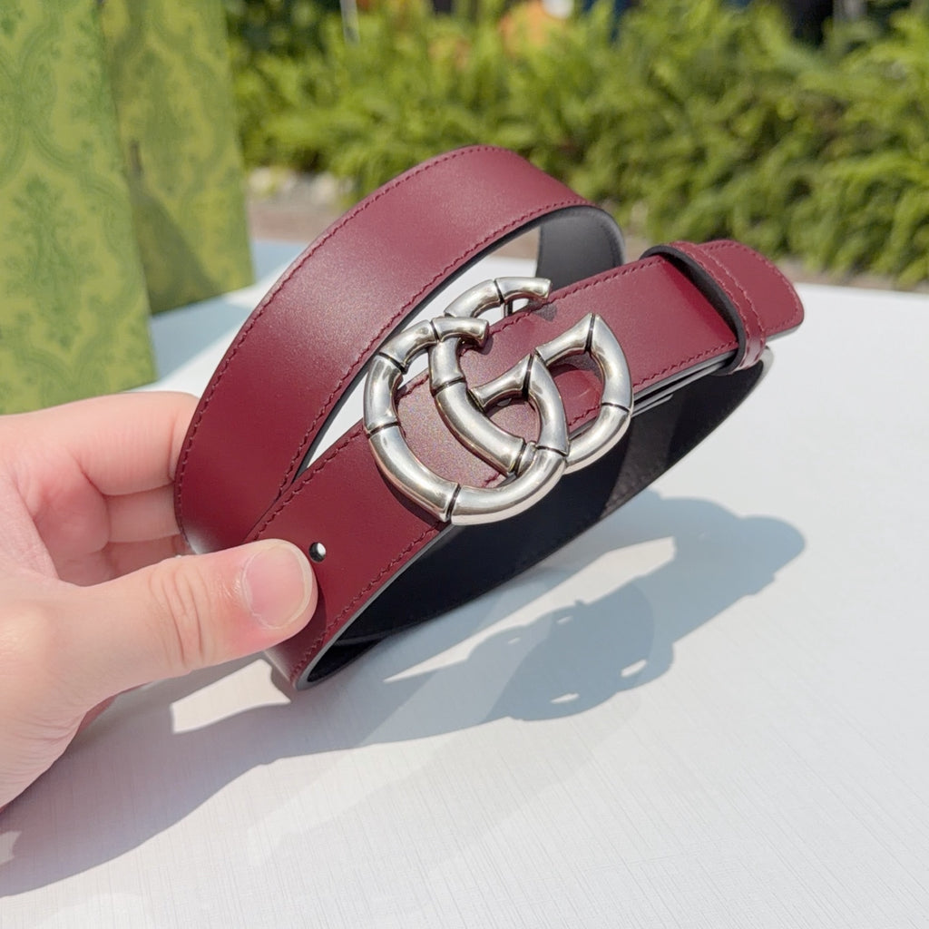 Gucci belt with wine red strap and silver buckle, held close by hand