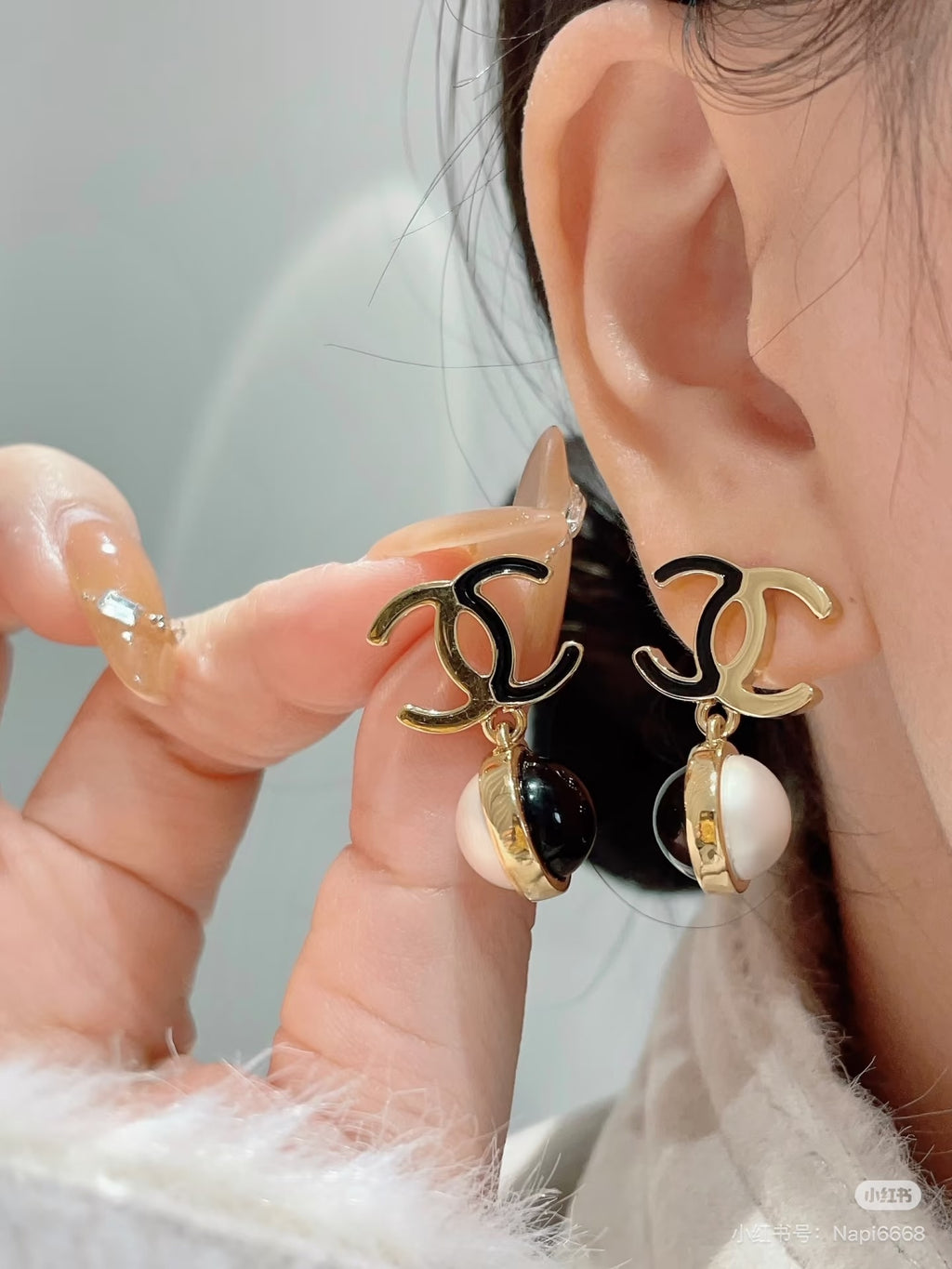 Gold-tone logo earrings with black and pearl drops near model ear
