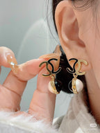 Gold-tone logo earrings with black and pearl drops near model ear