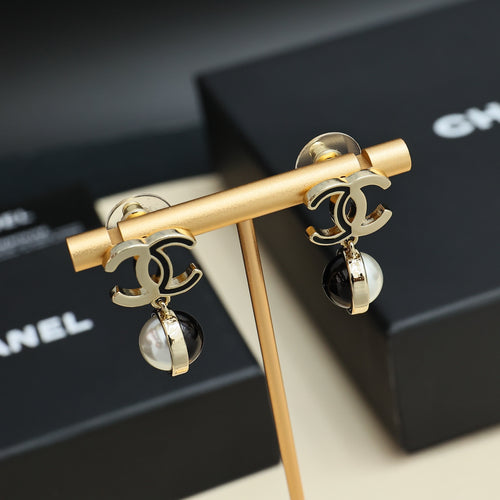 Gold-tone hoop earrings with pearl and black drop charms on stand