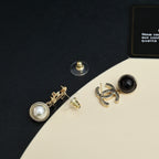 Gold-tone logo earrings with pearl and black drop pendants on dark card