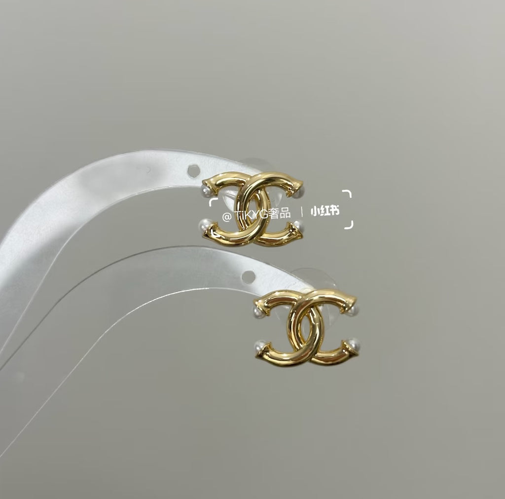 Chanel gold-tone CC logo earrings on white display with pearl-like bead accents