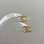 Chanel gold-tone CC logo earrings on white display with pearl-like bead accents