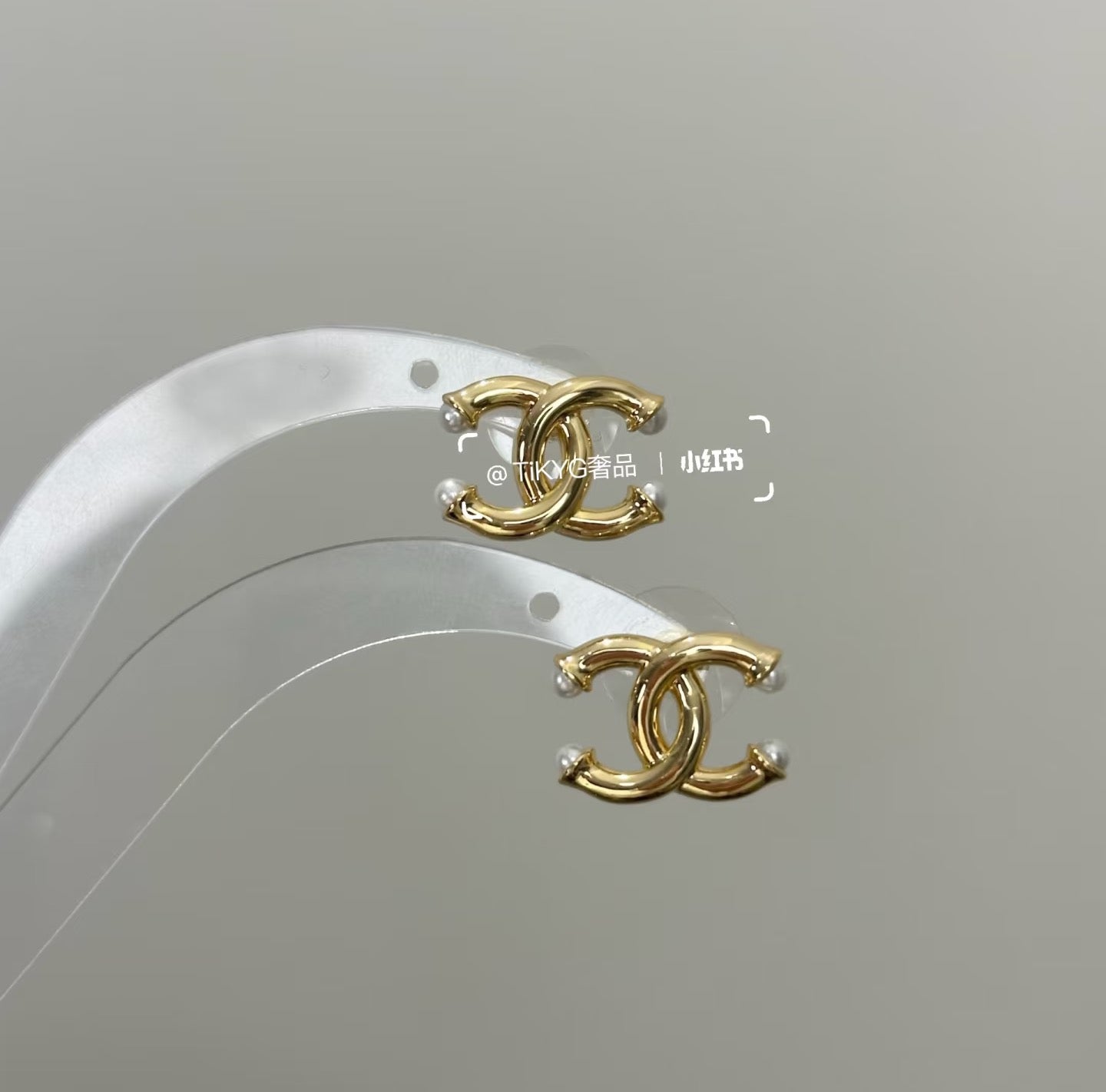 Chanel gold-tone CC logo earrings on white display with pearl-like bead accents