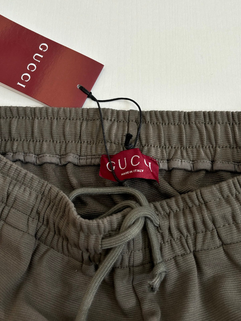 Dark gray Gucci shorts waistband with drawstring and logo; hanging brand tag