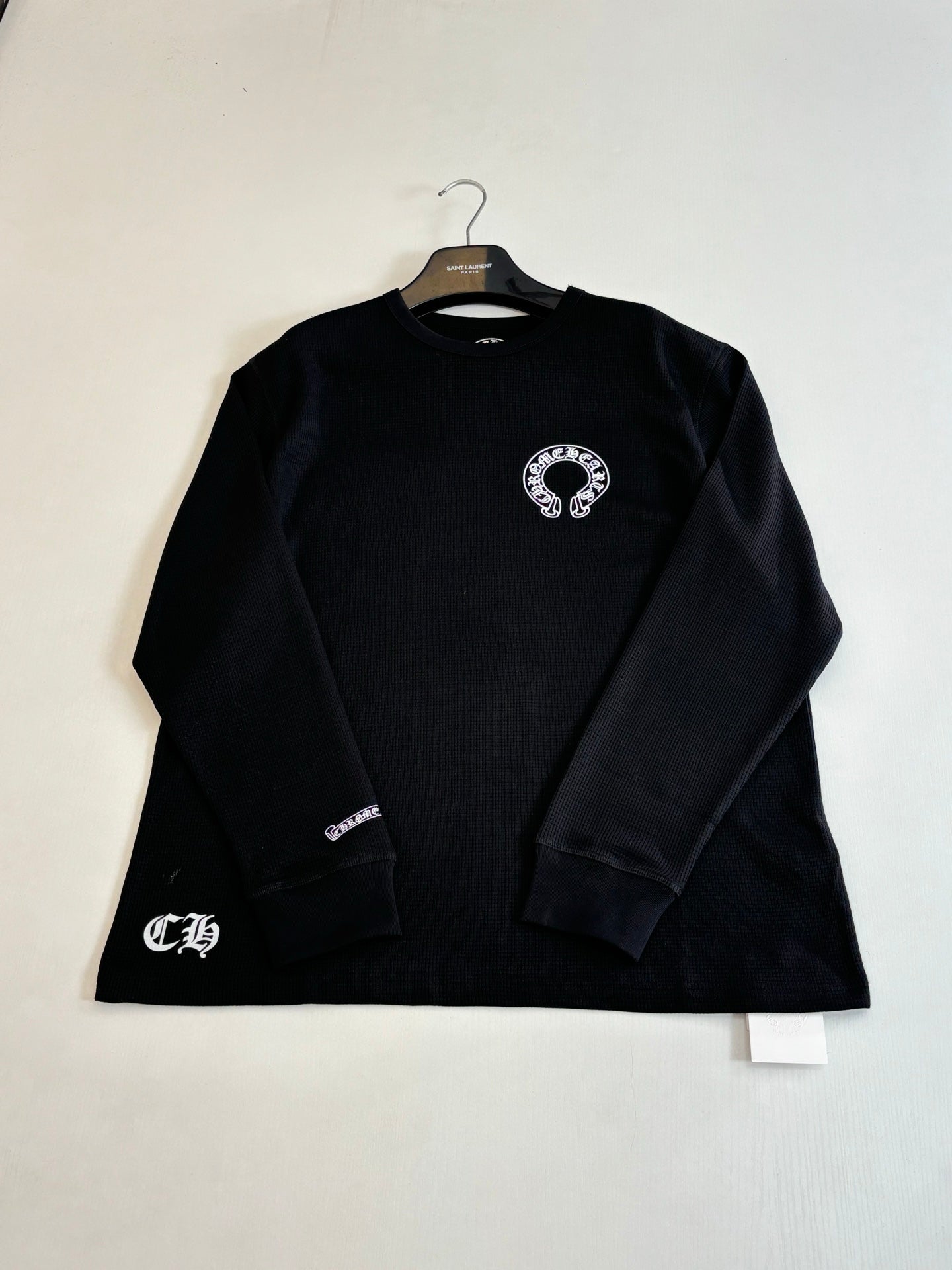 Black long-sleeve crewneck shirt with small front chest emblem and sleeve logo