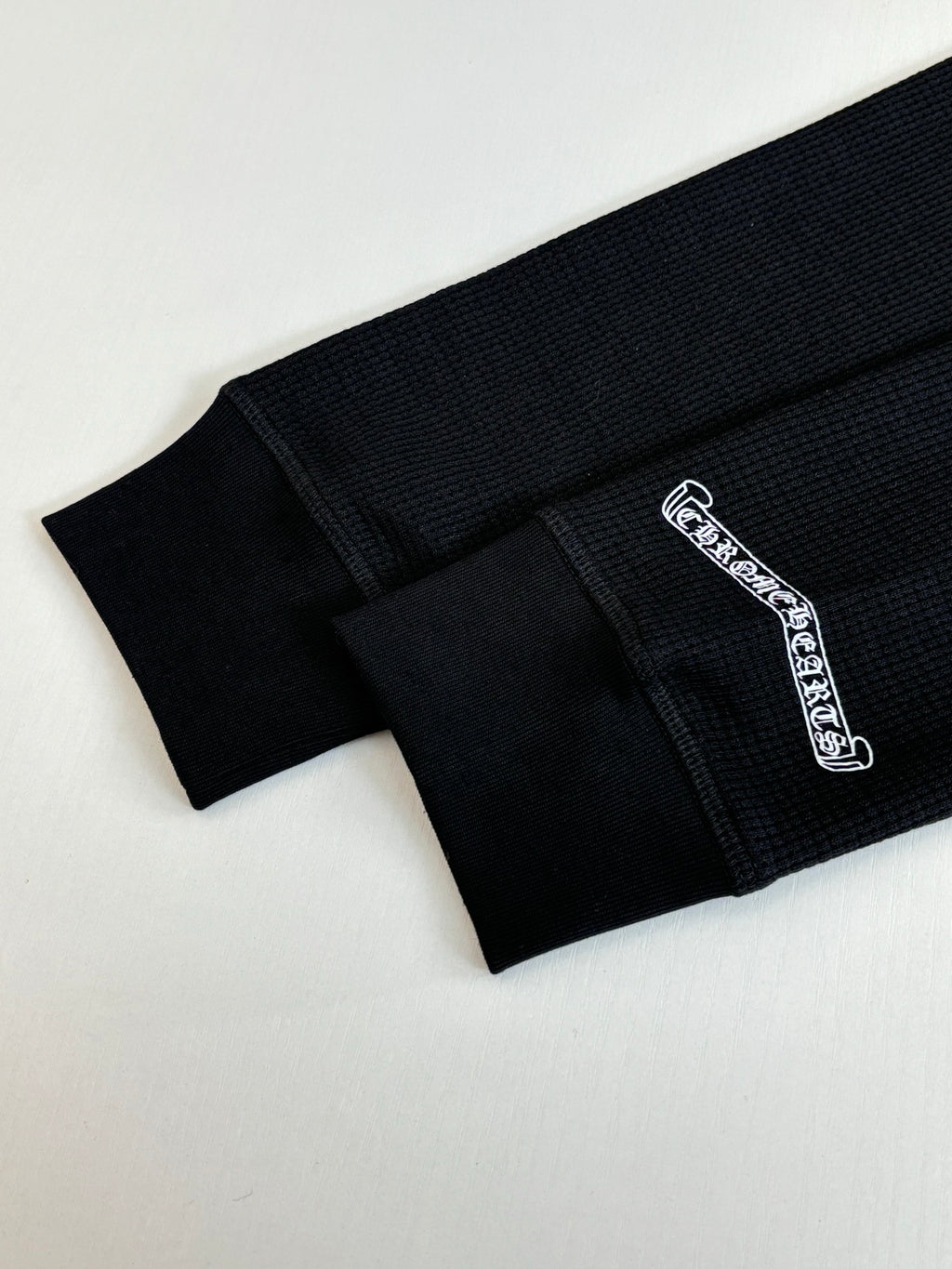 Black long-sleeve shirt with side cuff seam and white embroidered logo label