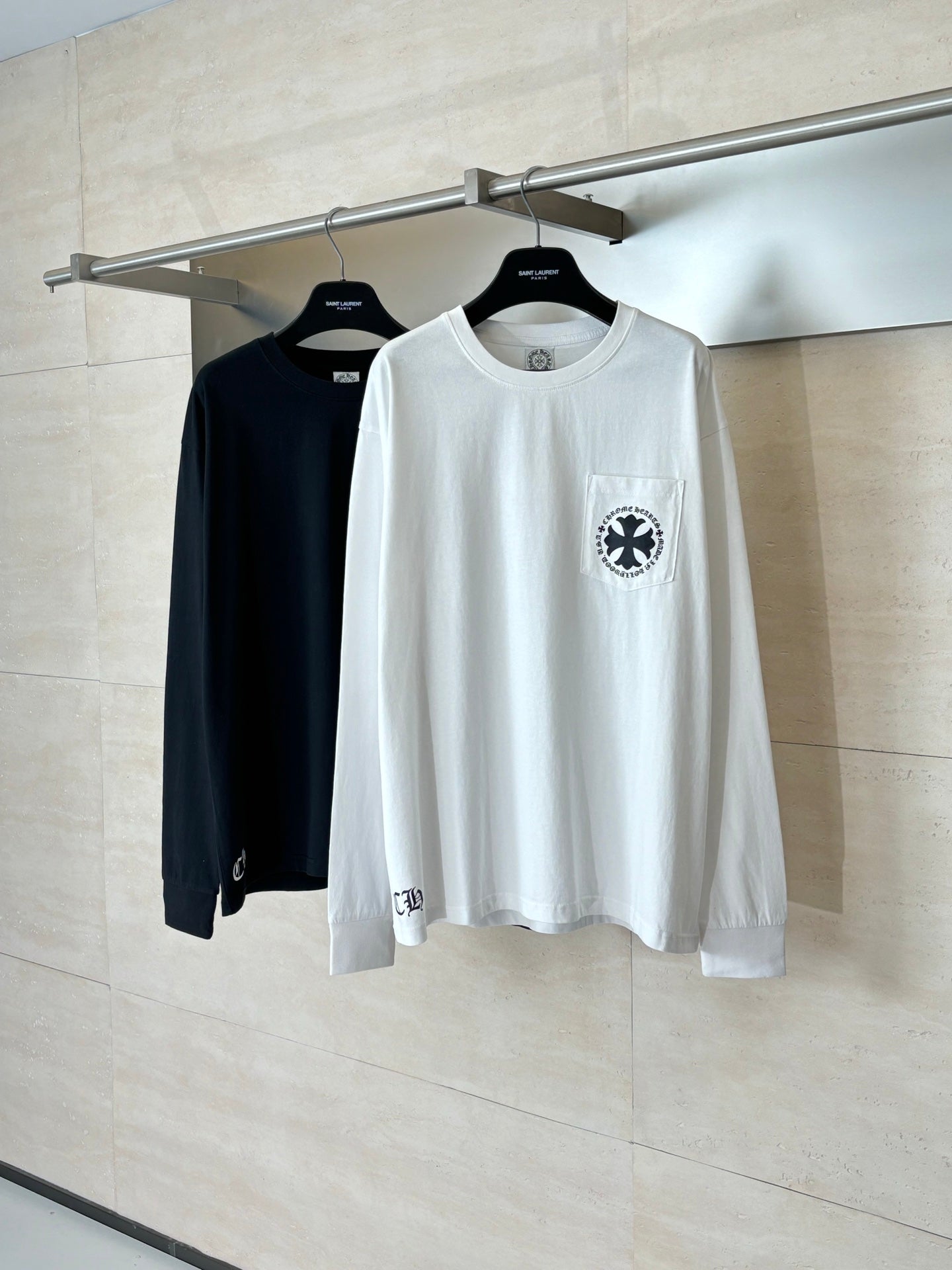 White and black long-sleeve T-shirts on hangers, each with a chest emblem.