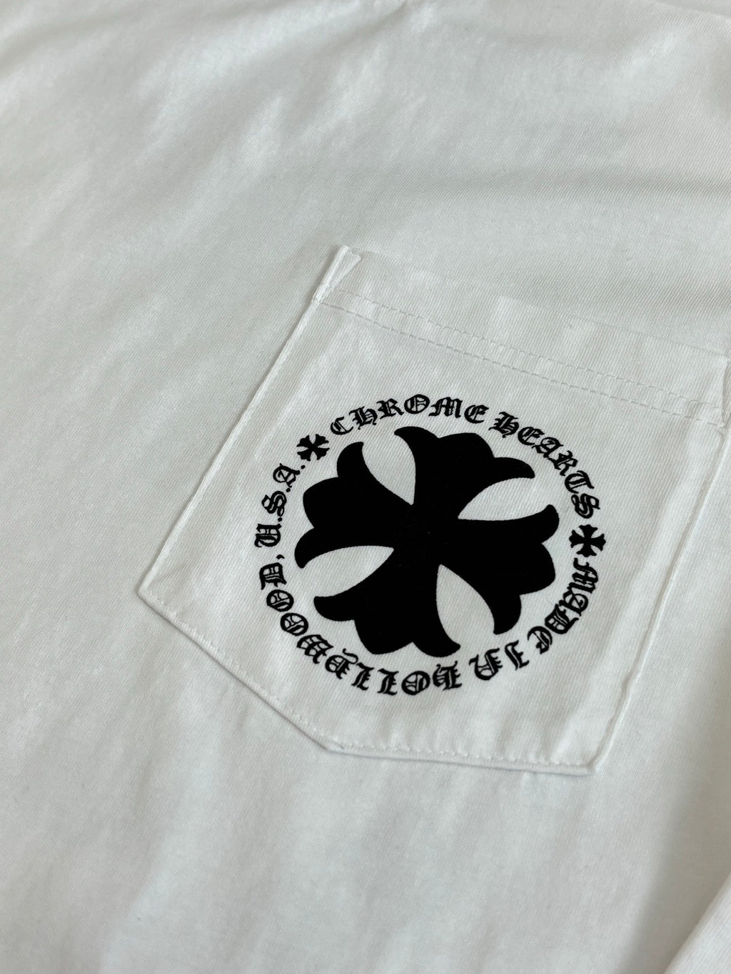White T-shirt pocket area with black cross emblem graphic.