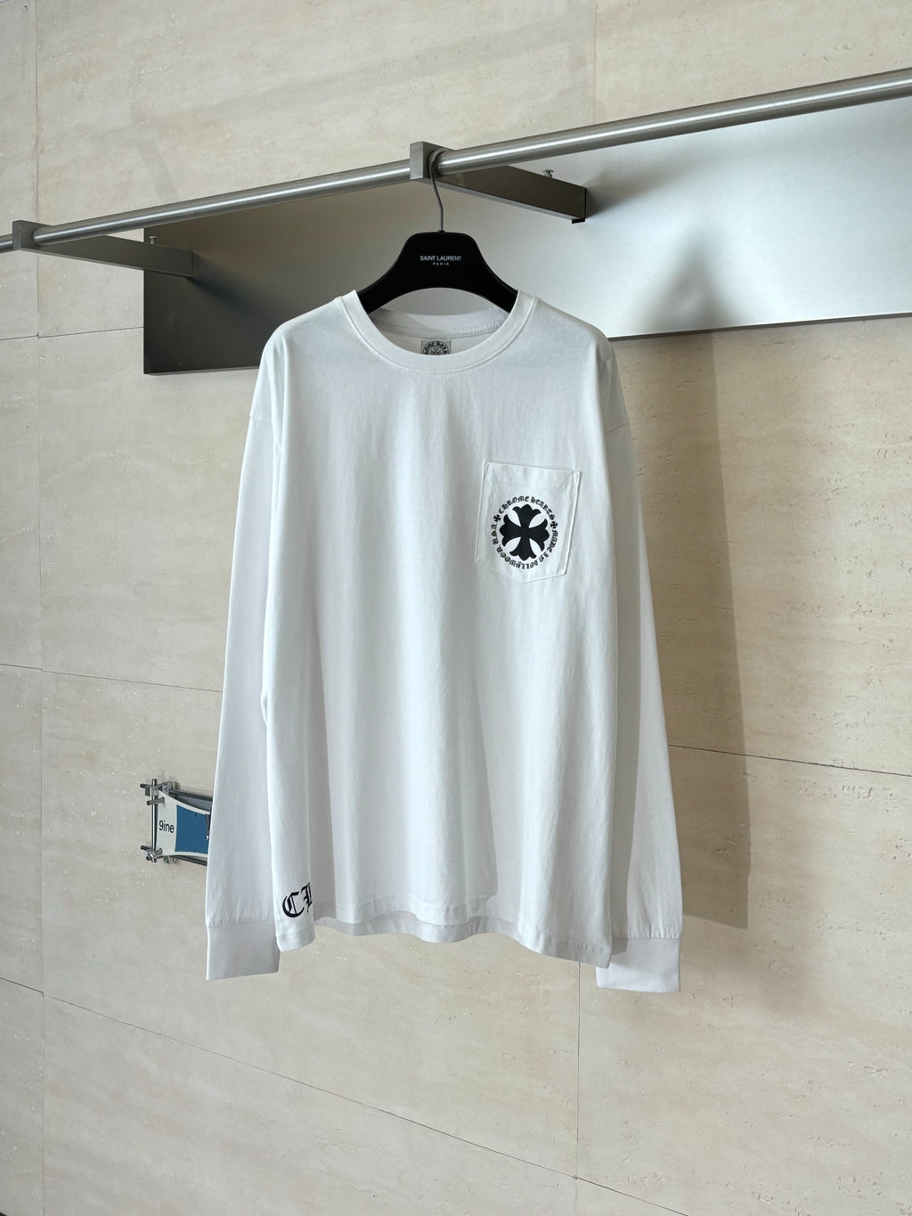 White long-sleeve T-shirt with circular black emblem on left chest.