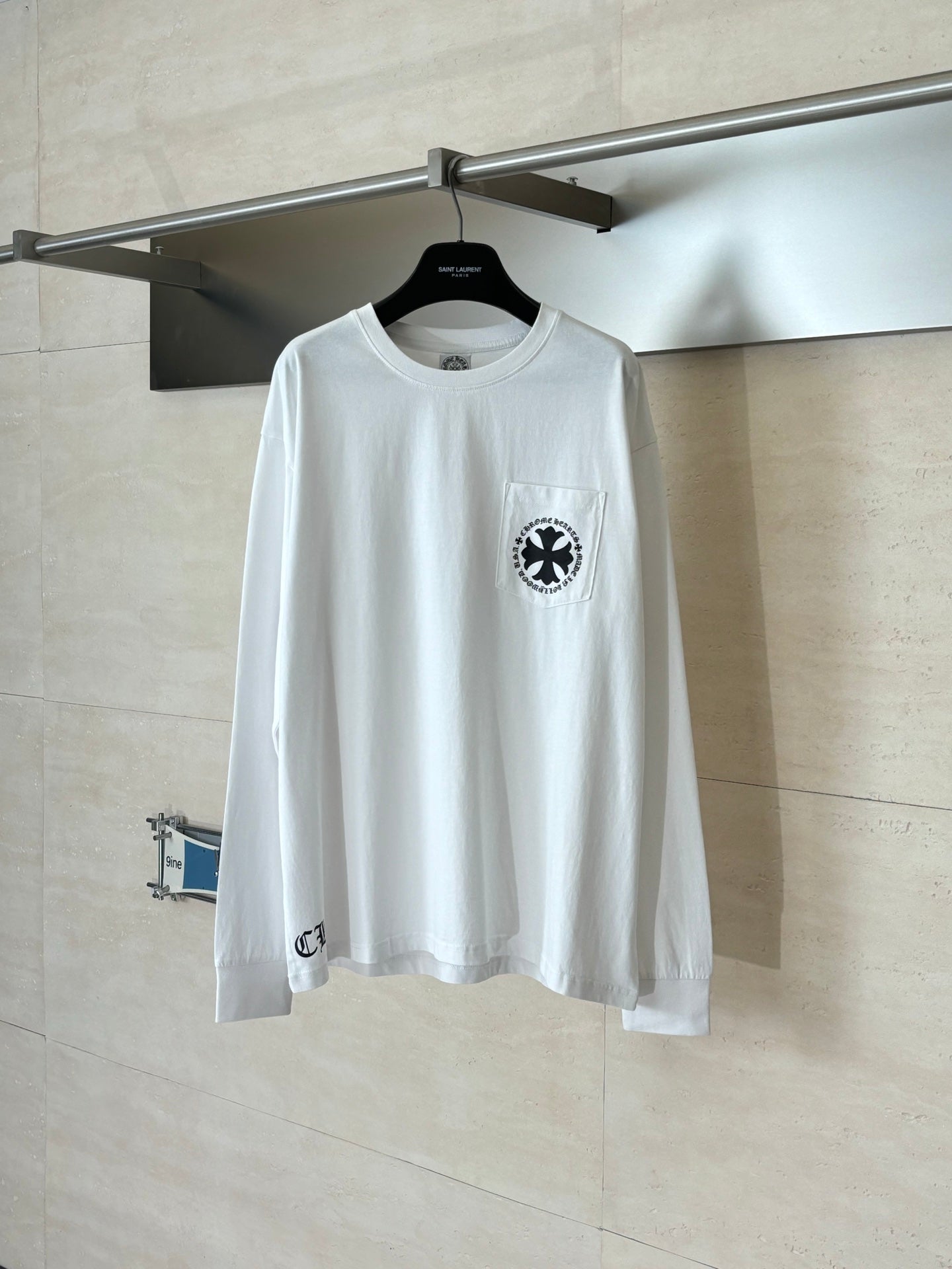 White long-sleeve T-shirt with circular black emblem on left chest.