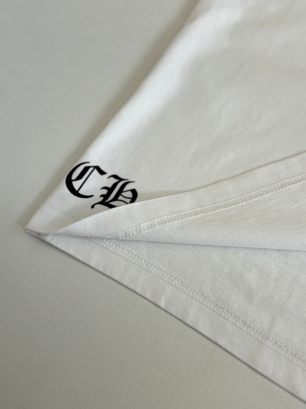 White T-shirt sleeve hem with black logo embroidery.