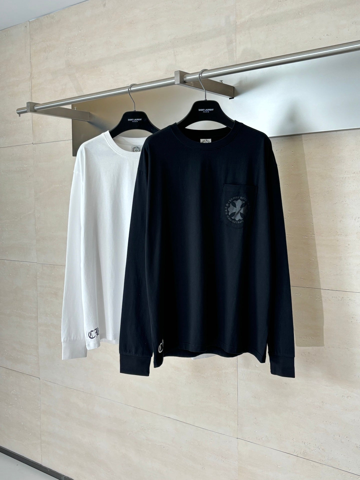 Two black and white long-sleeve crewneck tops on hangers