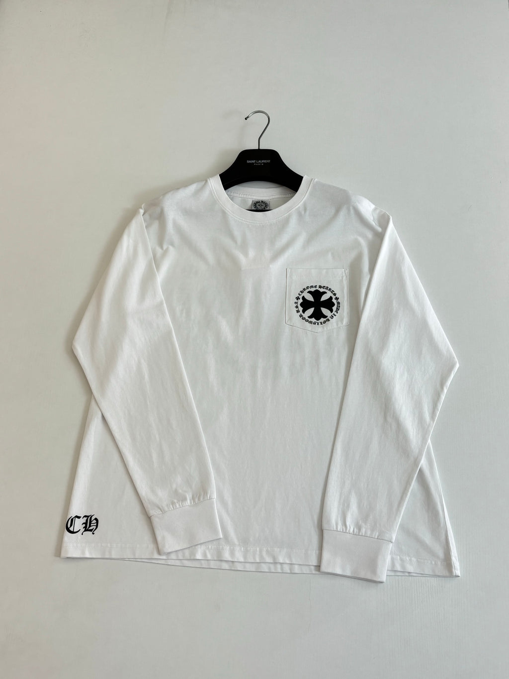 White long-sleeve T-shirt with small circular emblem on left chest.