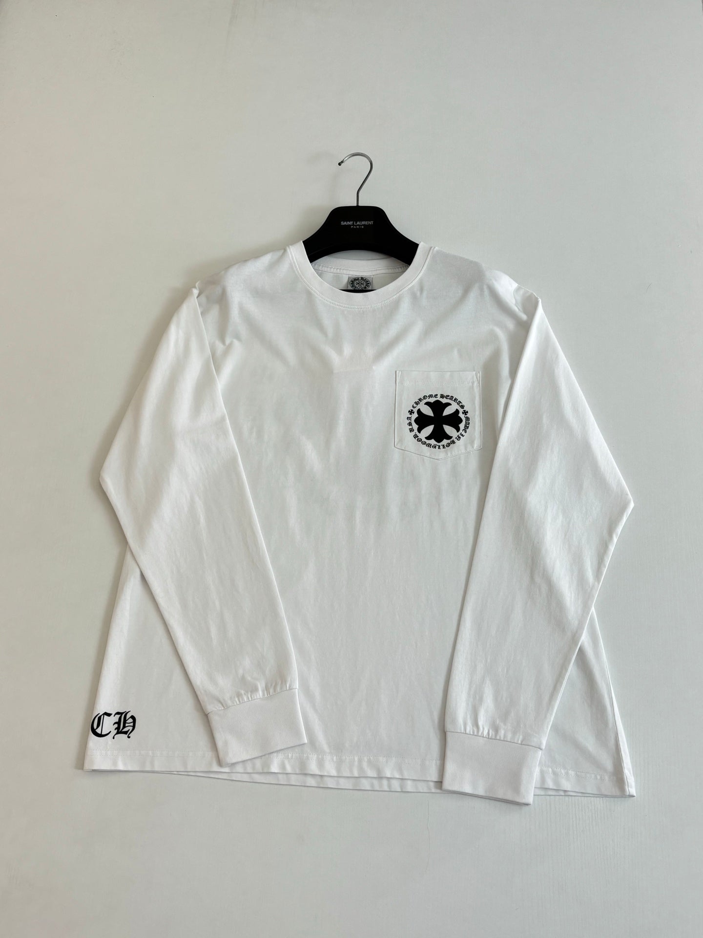 White long-sleeve T-shirt with small circular emblem on left chest.