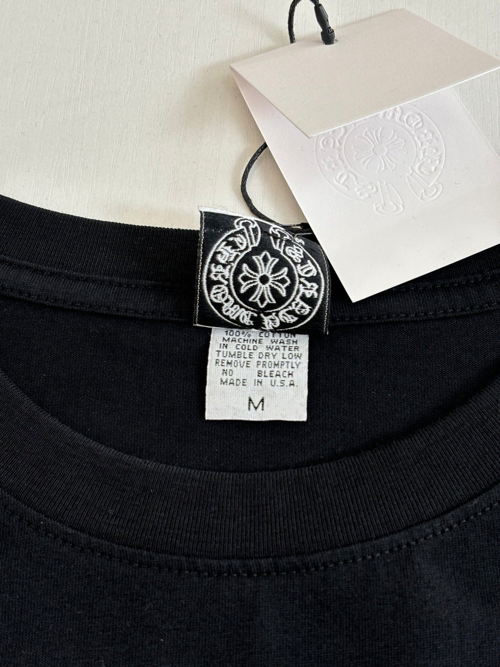 Black crewneck top neckline with size tag and logo patch