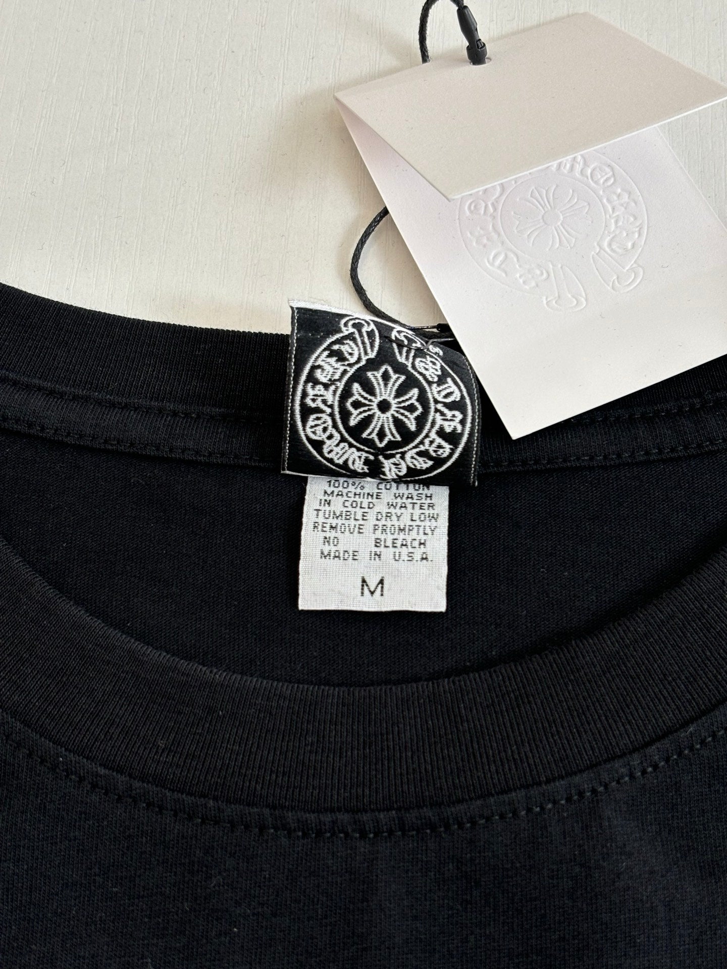 Black crewneck top neckline with size tag and logo patch