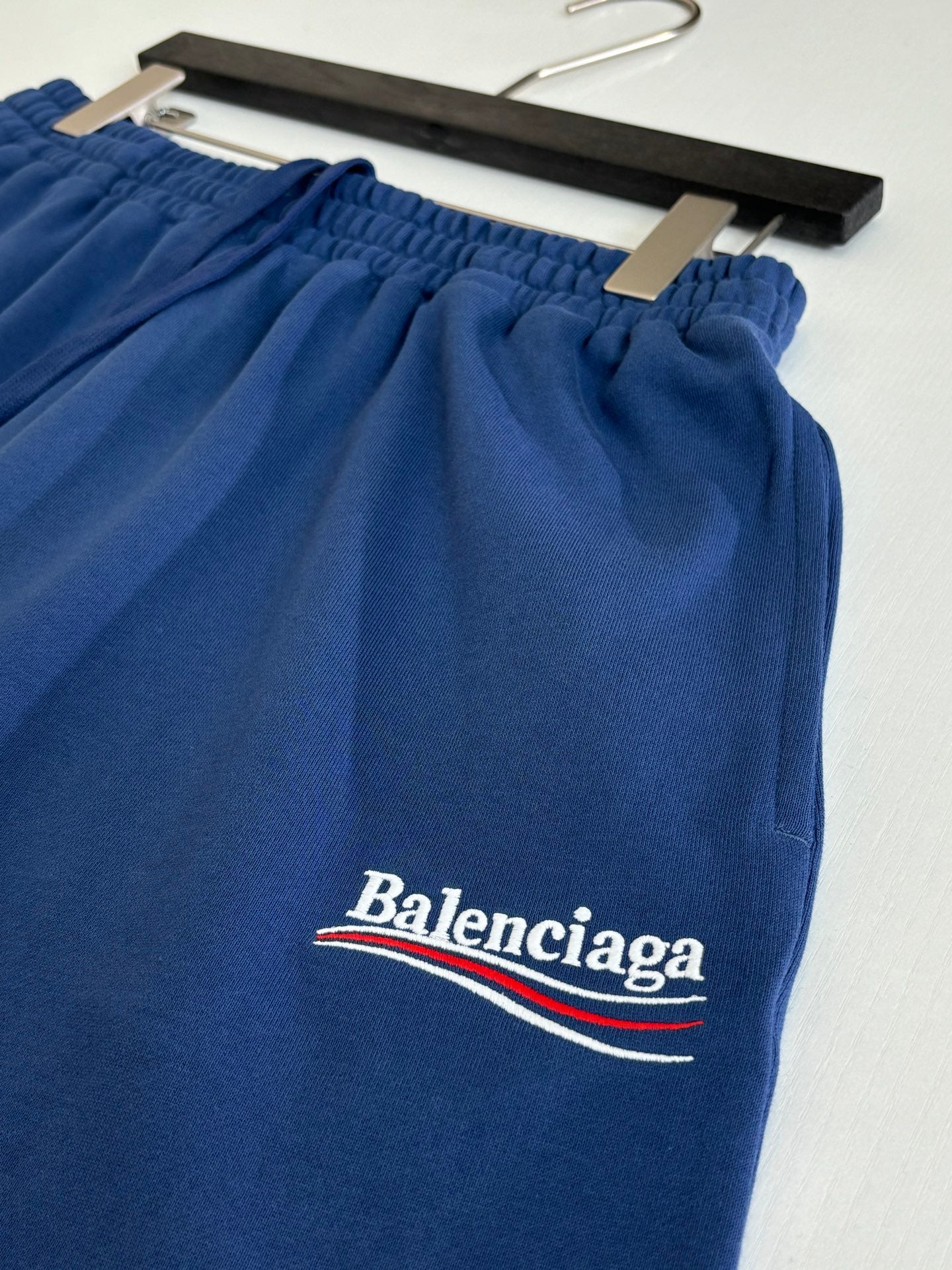Blue Balenciaga shorts with logo on hem, shown on hanger