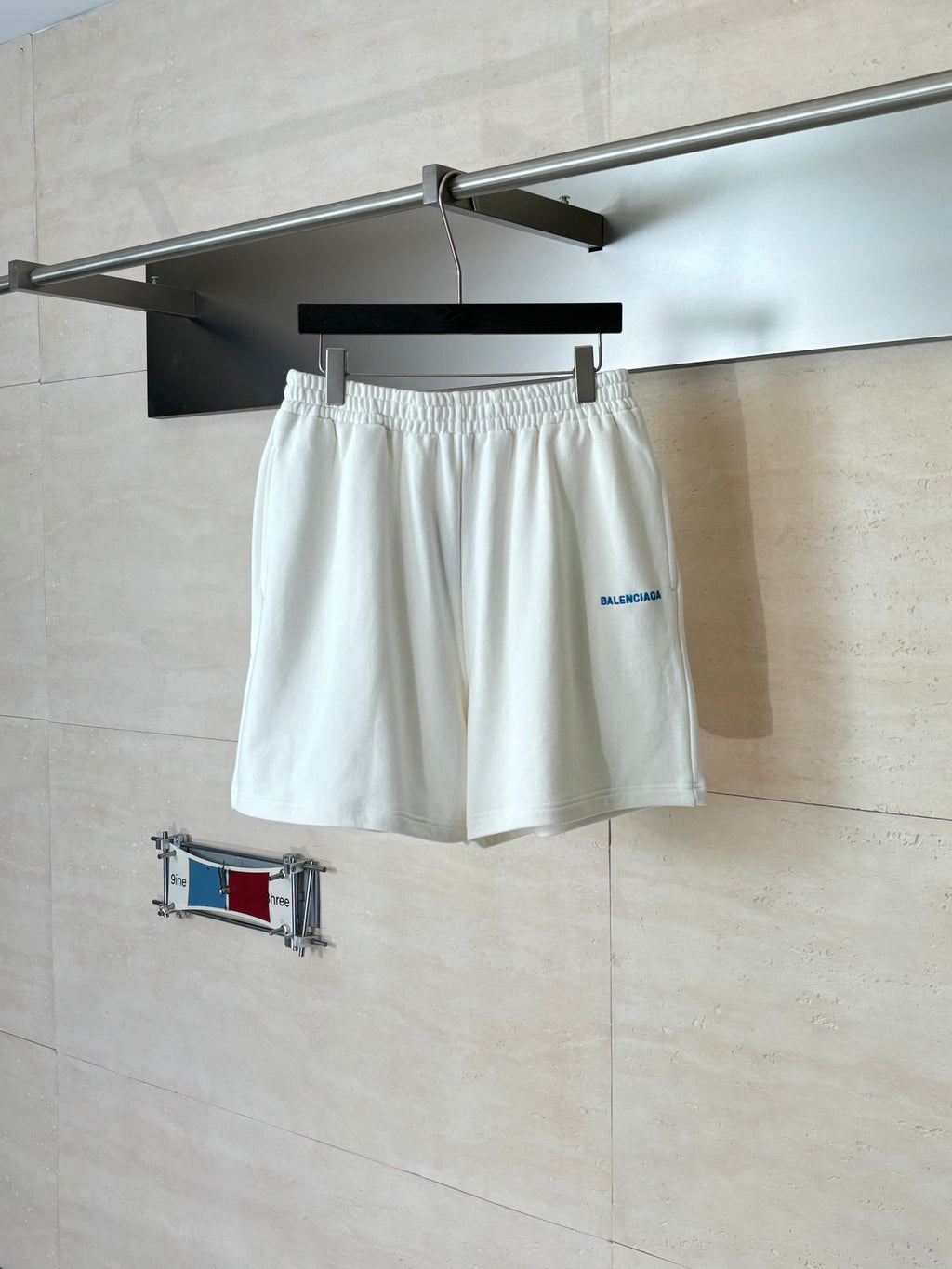 White Balenciaga shorts with elastic waistband and small blue logo on front.