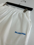 White Balenciaga shorts close-up with elastic waistband and blue BALENCIAGA logo print.
