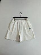 White Balenciaga shorts on hanger with elastic waistband and blue logo on leg.