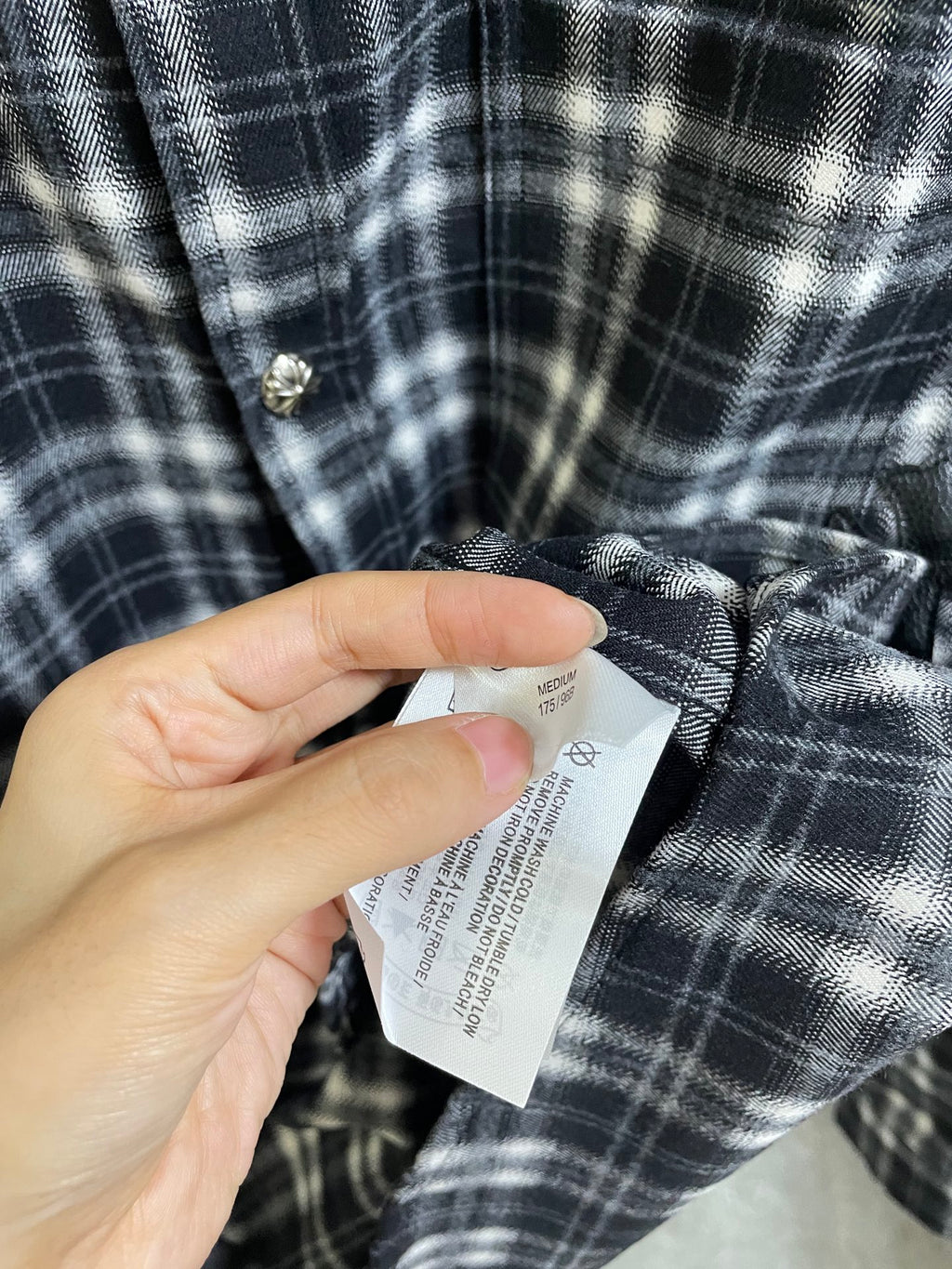 Hand holding a care label on black-and-white plaid long-sleeve button-up