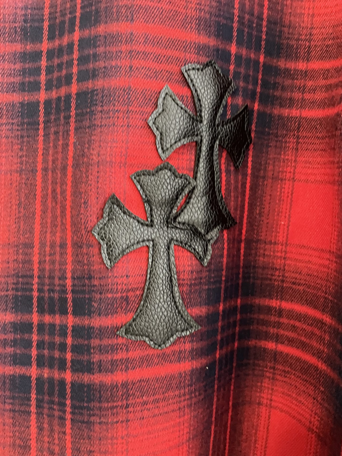 Red plaid shirt with dark embroidered cross emblem on front