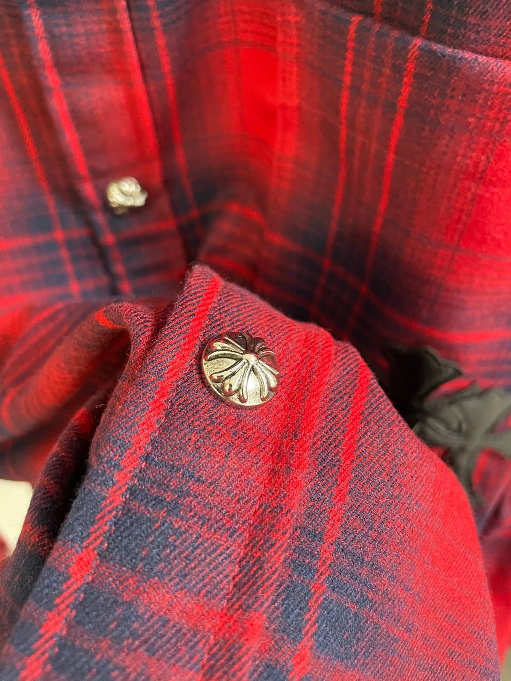 Red plaid shirt collar close-up with gold-toned button and round emblem