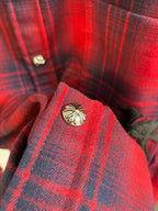 Red plaid shirt collar close-up with gold-toned button and round emblem