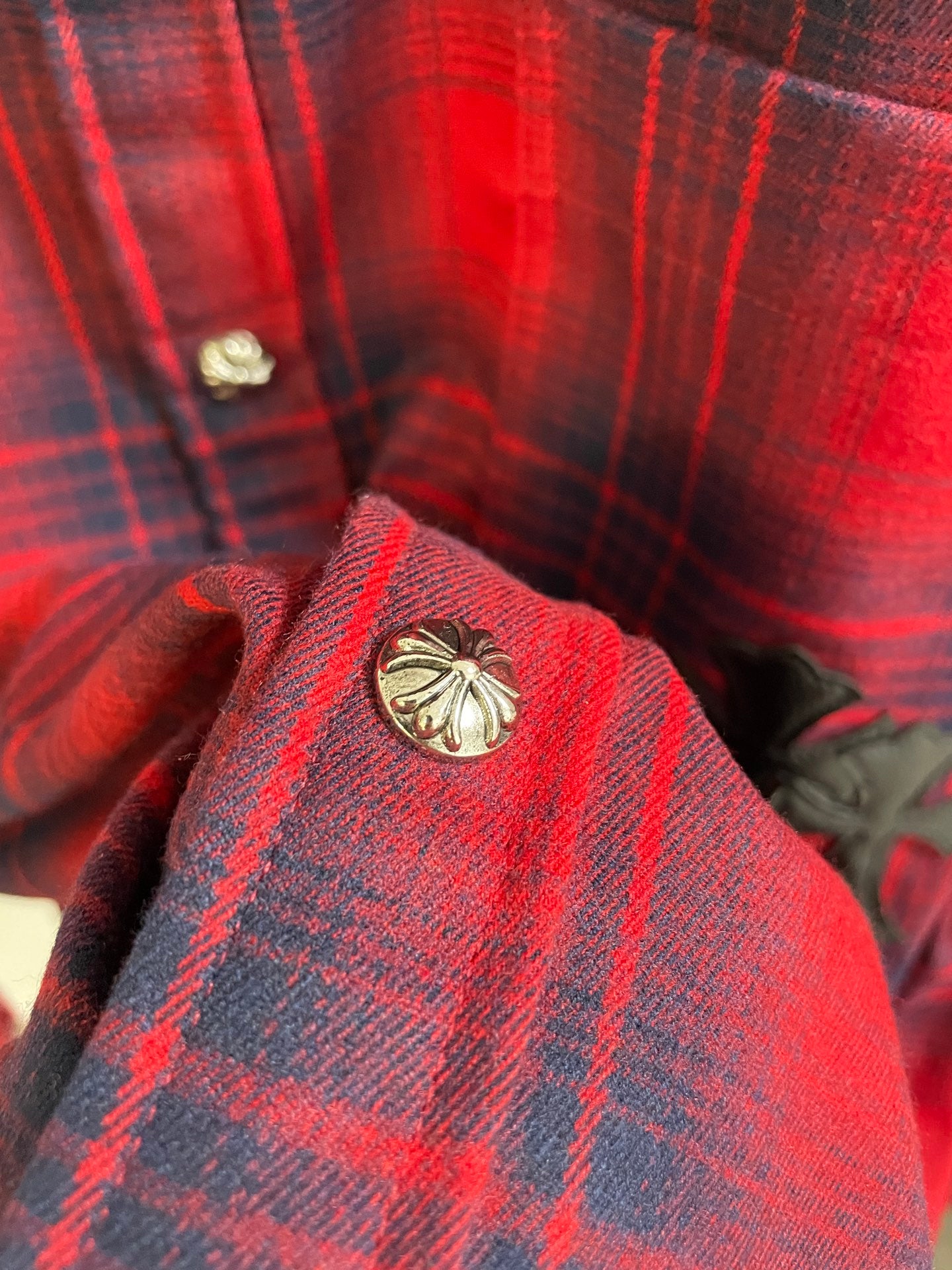 Red plaid shirt collar close-up with gold-toned button and round emblem