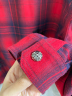 Red plaid shirt cuff with decorative snap button and embroidered emblem