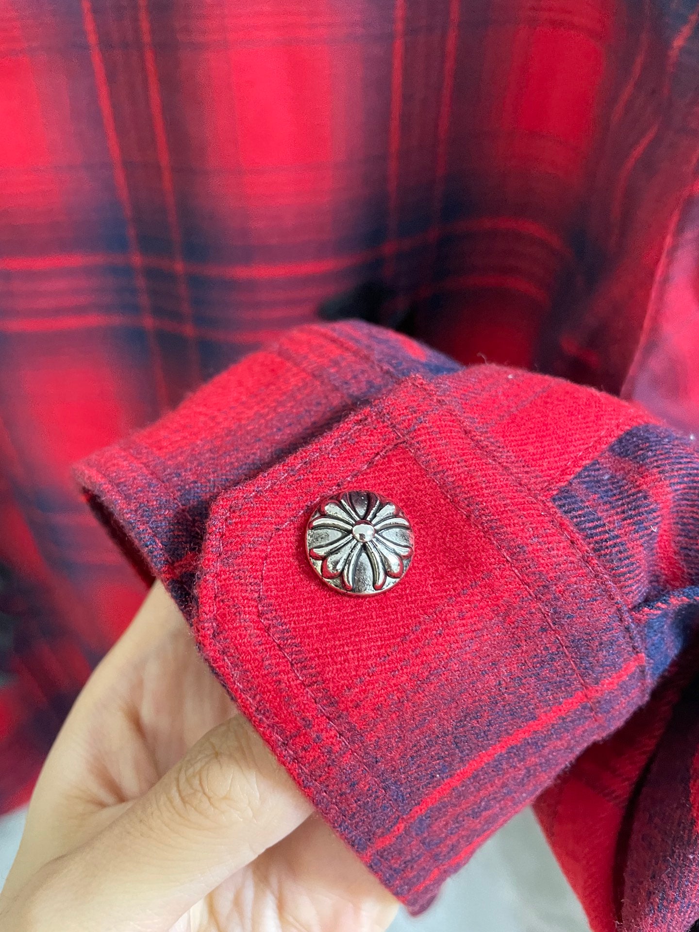 Red plaid shirt cuff with decorative snap button and embroidered emblem