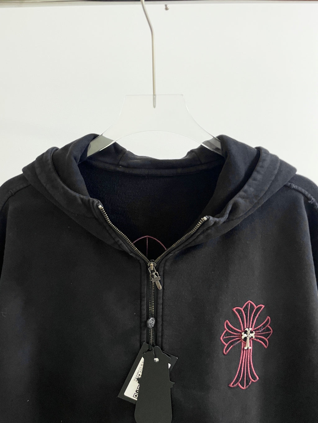 Dark zip hoodie with hood, red cross emblem, and gold zipper pull