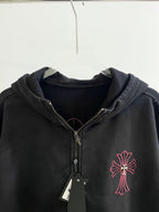 Dark zip hoodie with hood, red cross emblem, and gold zipper pull