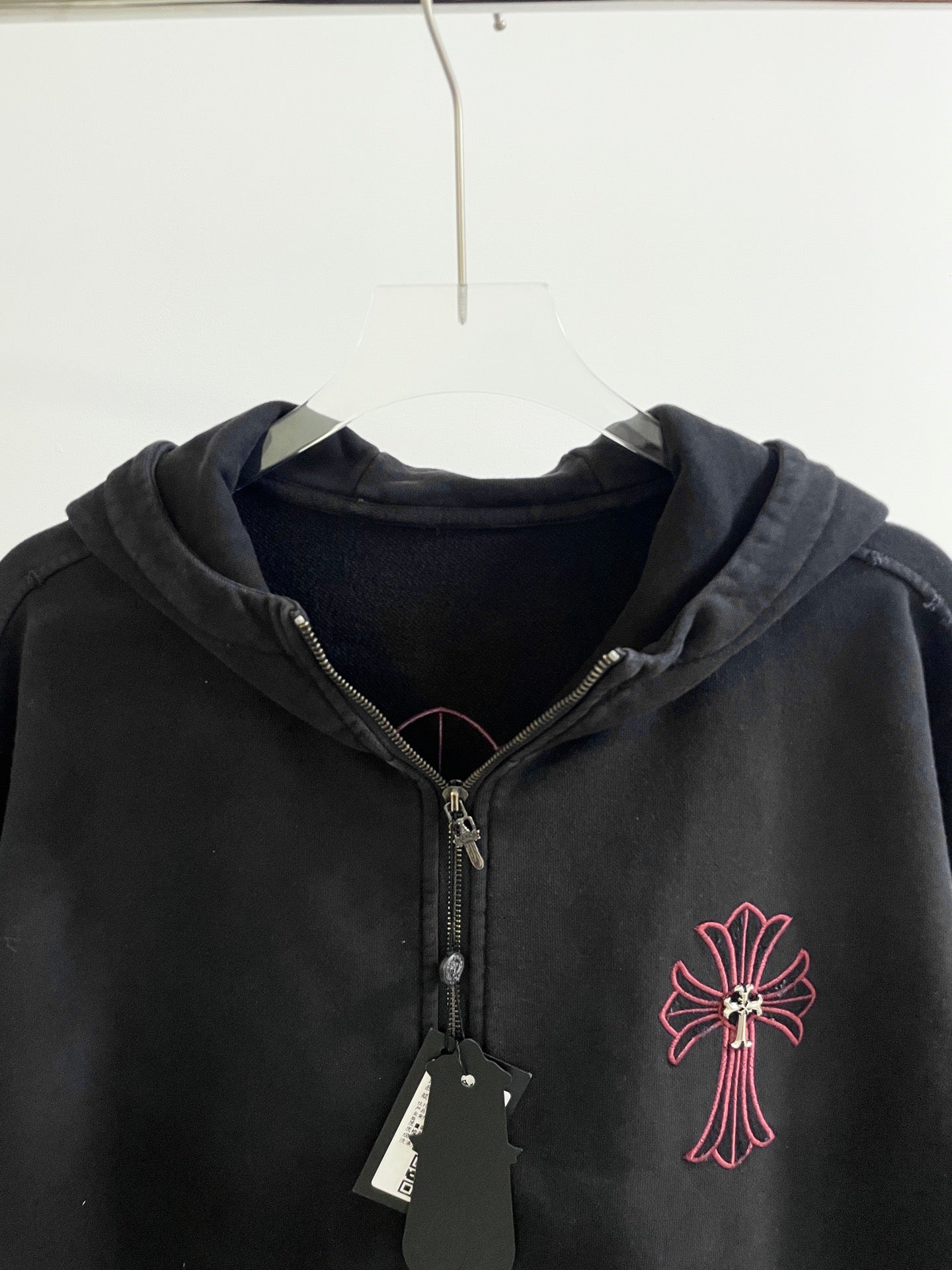 Dark zip hoodie with hood, red cross emblem, and gold zipper pull