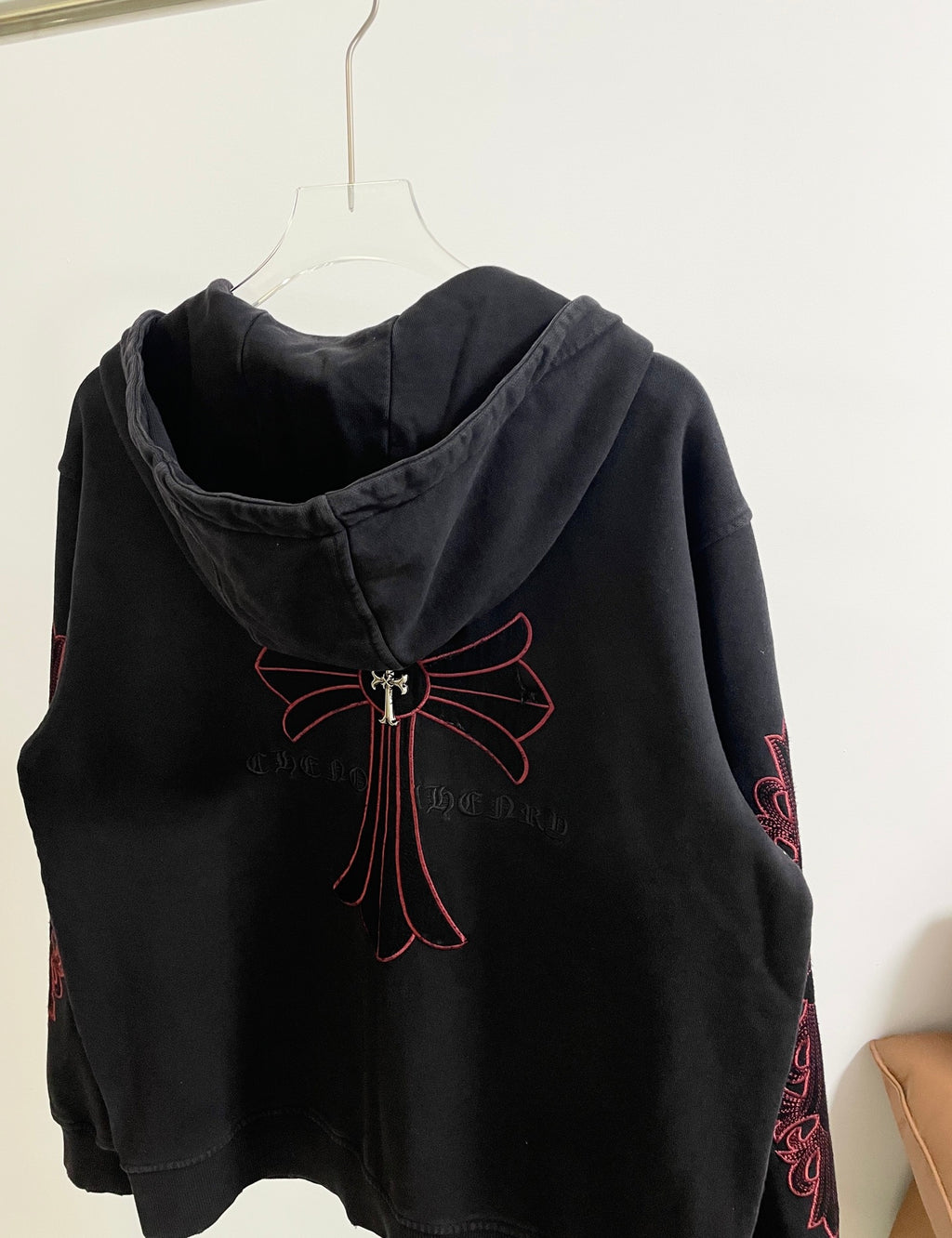 Dark hoodie with hood and red cross-bow emblem on upper back