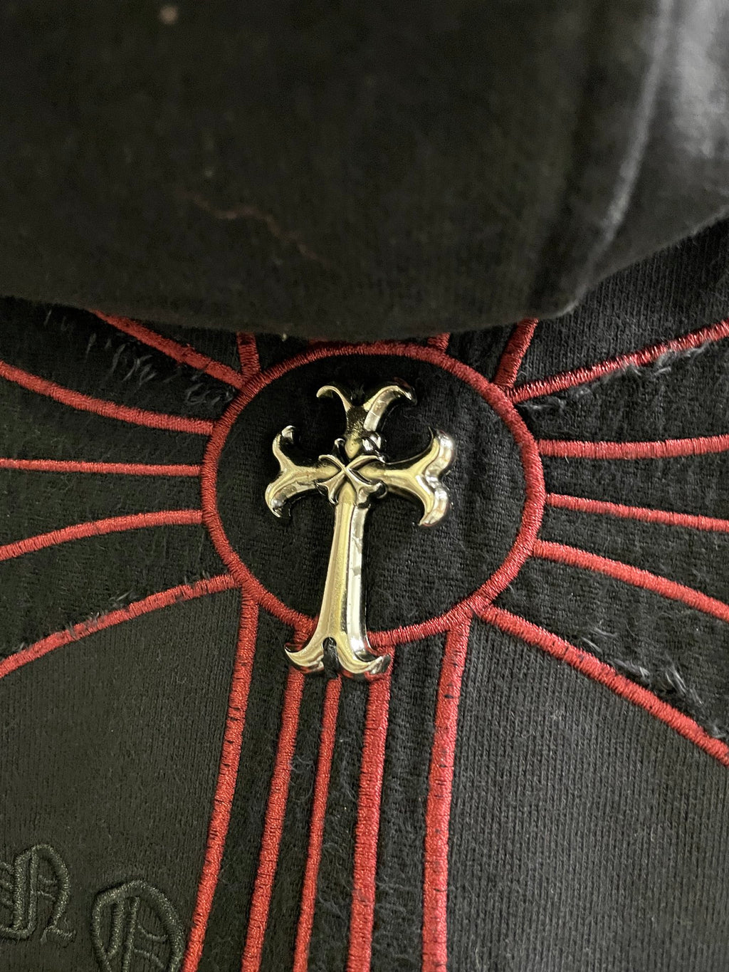 Dark hoodie cross emblem with gold center and red stitched rays