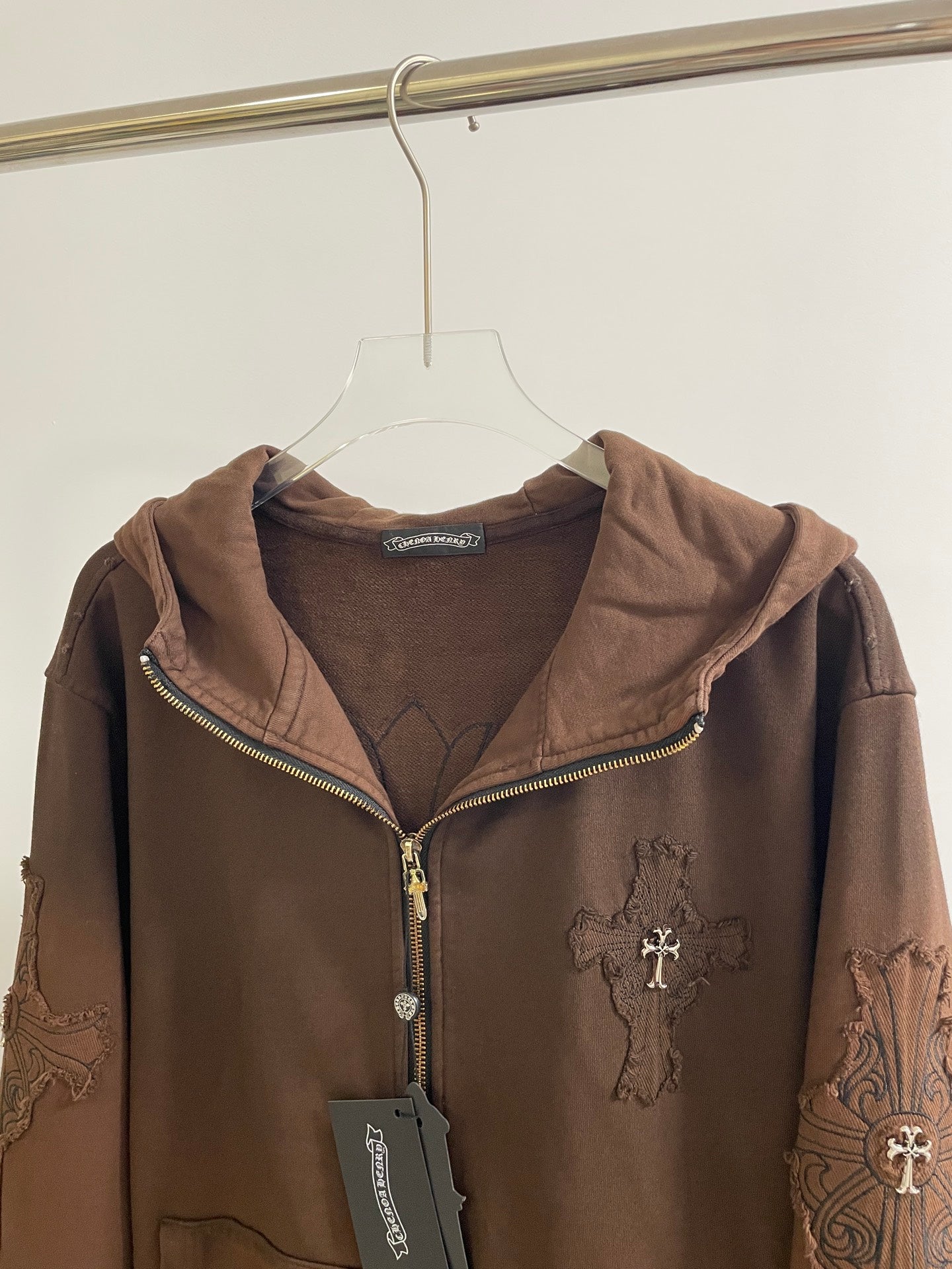 Zip-up hooded jacket close-up, brown, with front zipper and embroidered cross graphic