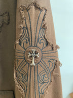 Embroidered cross emblem with blue ornamental lines on tan fabric