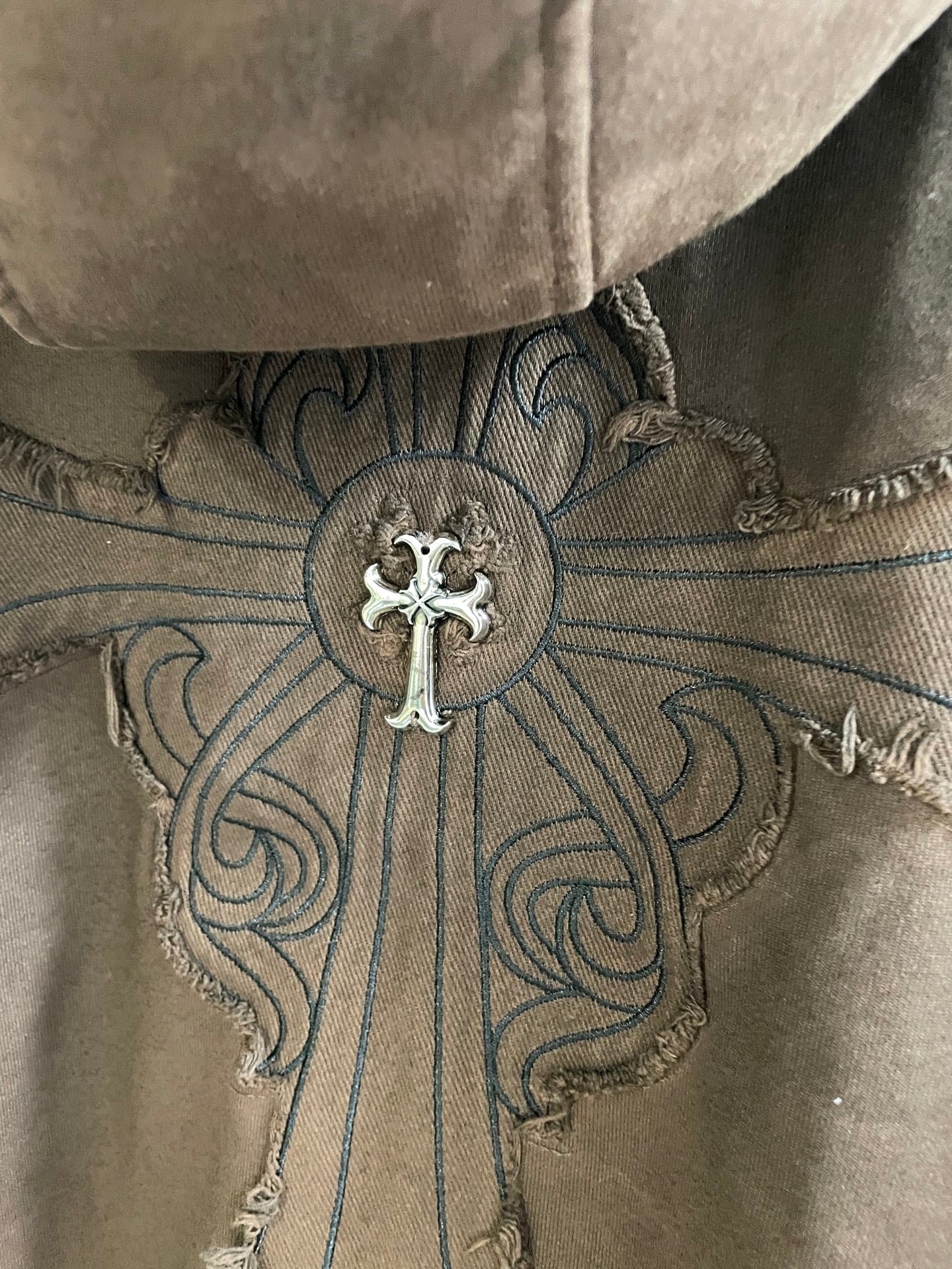 Brown hoodie back yoke with large cross emblem and ornate embroidered swirls