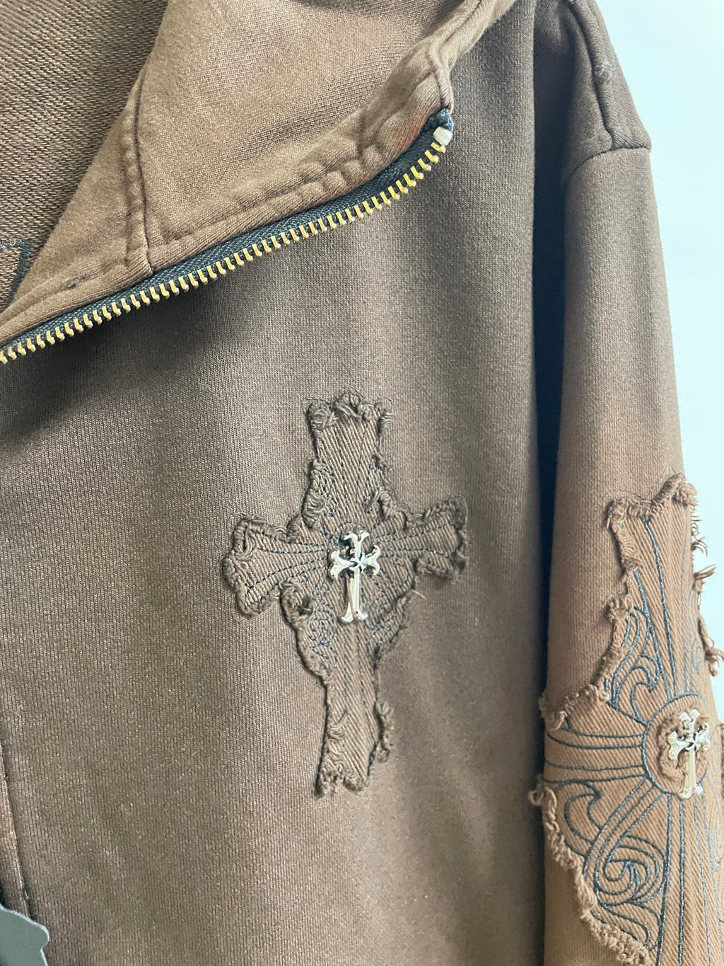 Brown hoodie sleeve with cross applique and embroidered swirl pattern