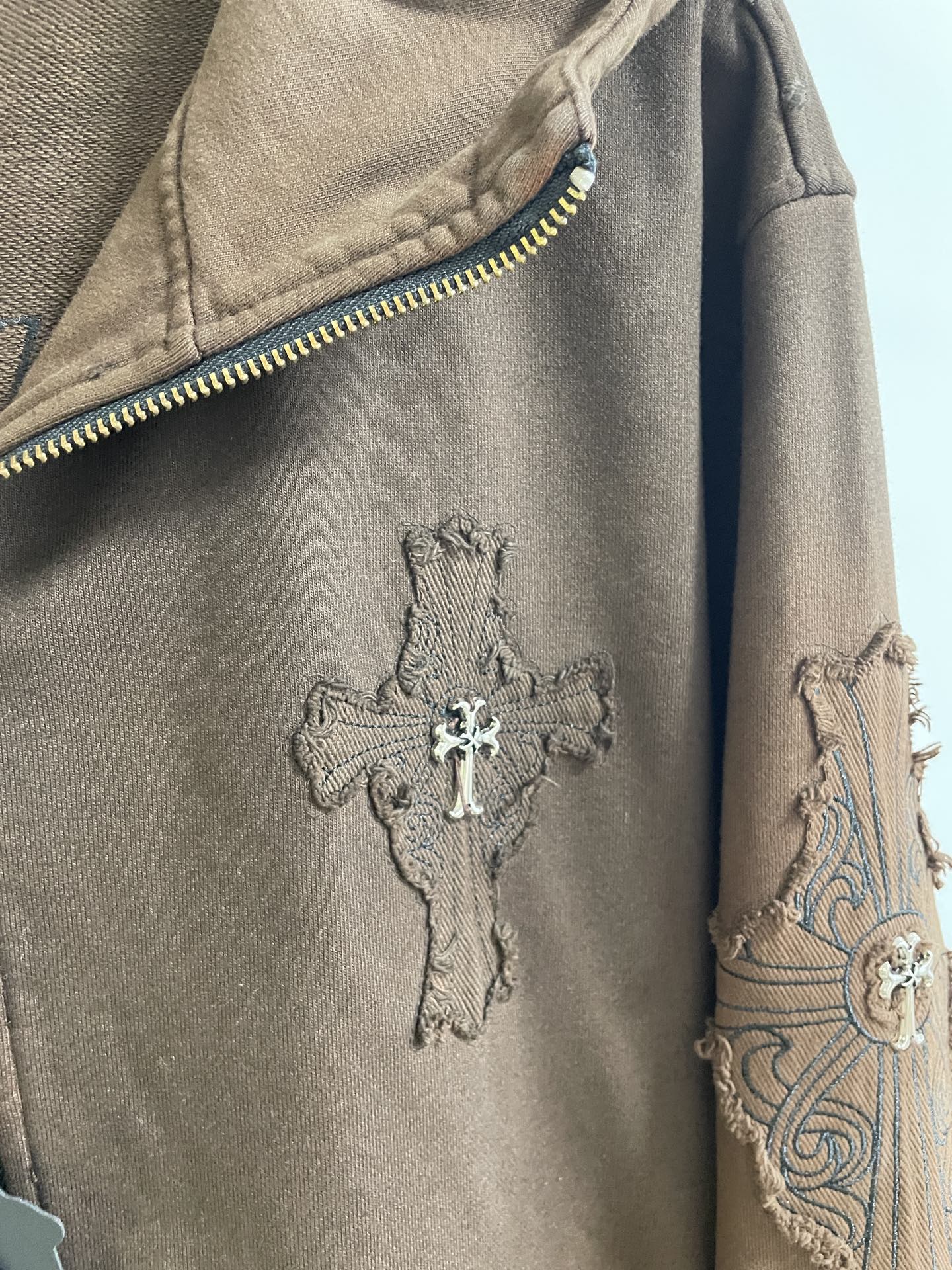 Brown hoodie sleeve with cross applique and embroidered swirl pattern