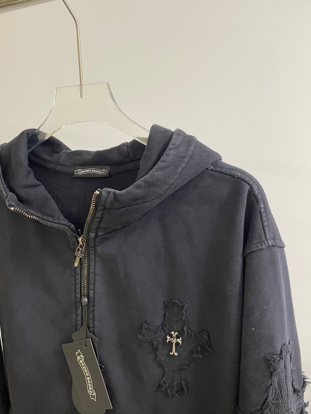 Dark hoodie jacket with zip front, hood, ribbed cuffs, and cross emblem at chest