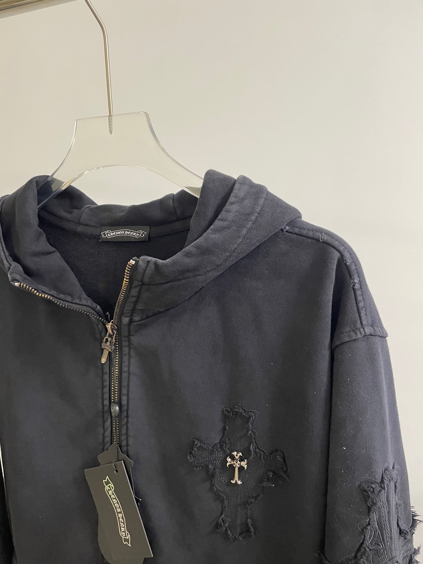 Dark hoodie jacket with zip front, hood, ribbed cuffs, and cross emblem at chest