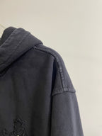 Dark hoodie with hood and textured shoulder panel featuring a small cross patch
