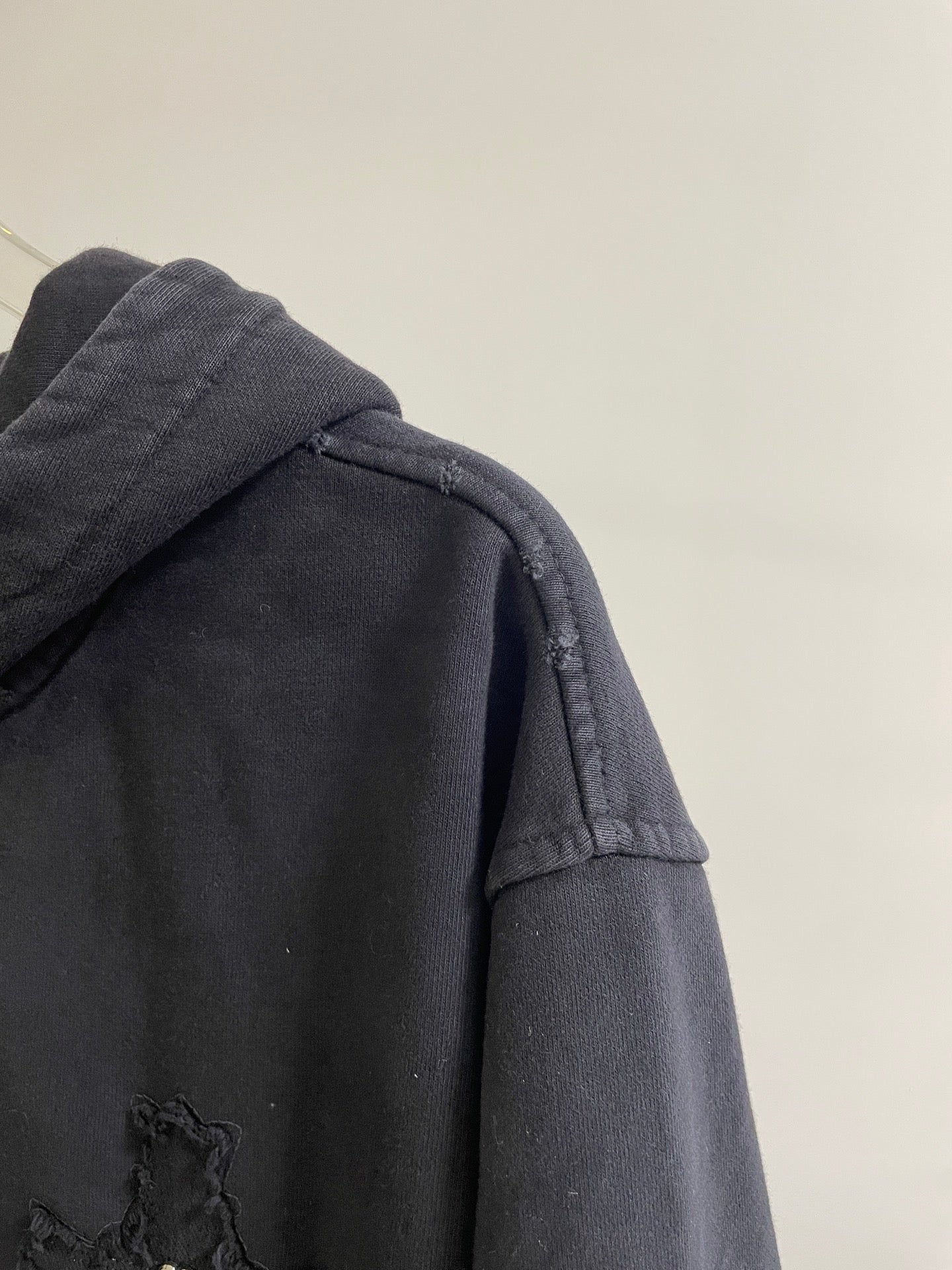 Dark hoodie with hood and textured shoulder panel featuring a small cross patch
