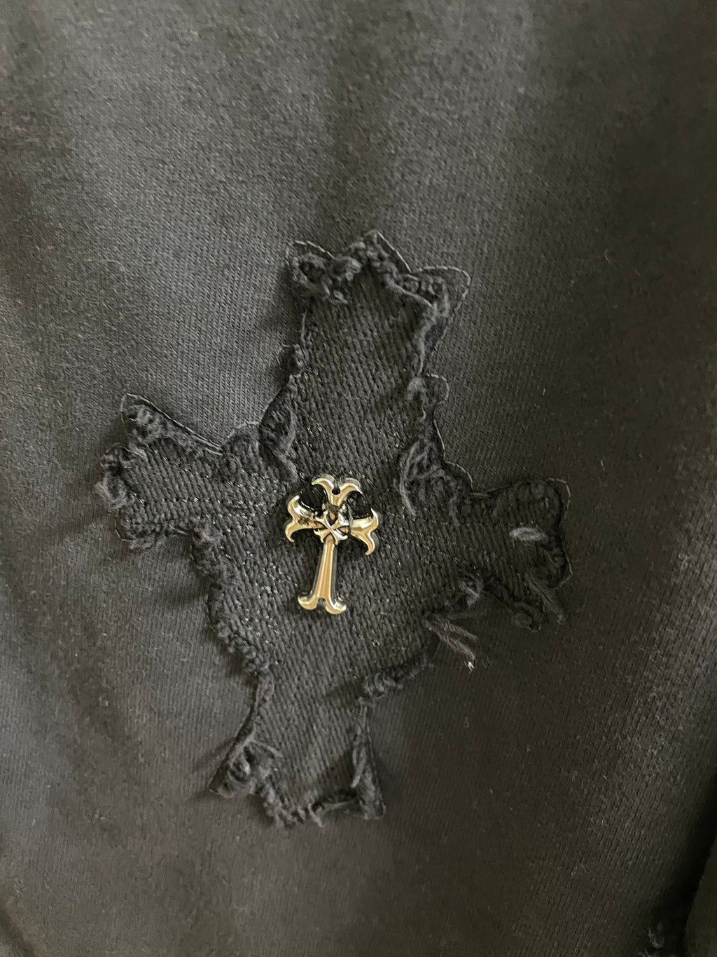 Close-up of dark fabric with stitched cross graphic and small embroidered accents
