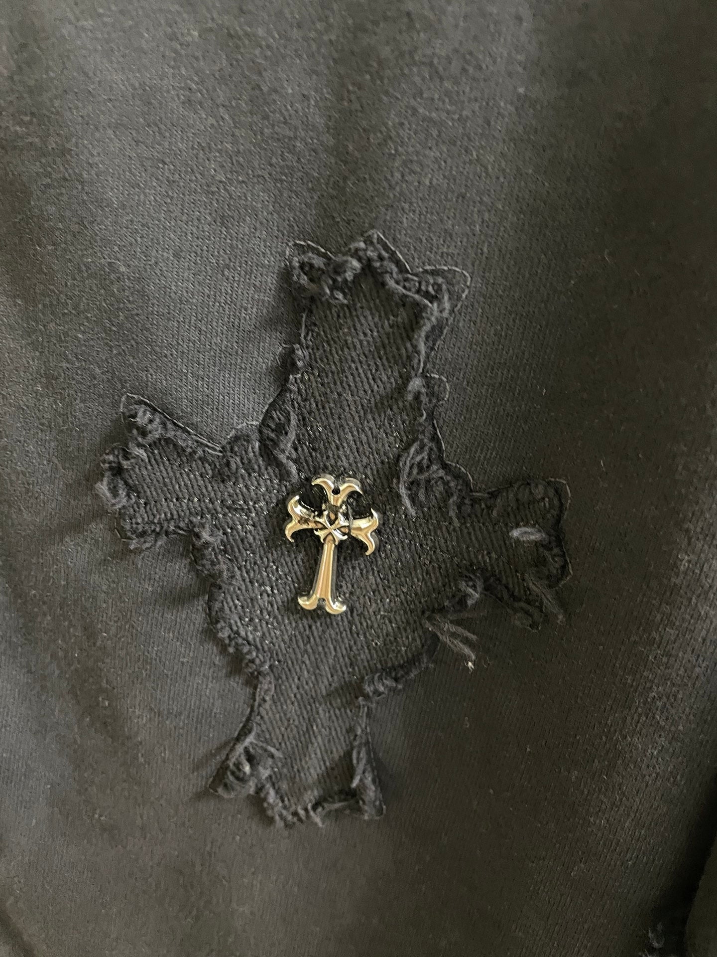 Close-up of dark fabric with stitched cross graphic and small embroidered accents